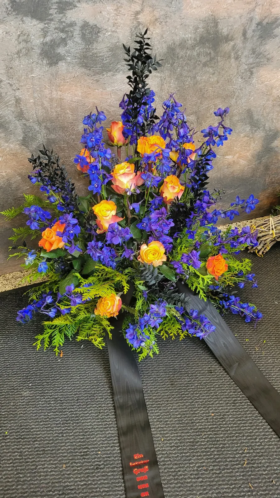 Trauergesteck mit blauen und orangefarbenen Blüten. Pusteblume Halle